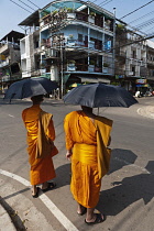 Laos, Vientiane, Two monks, shielded from sun by umbrellas, about to cross the street.