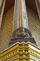 Thailand, Bangkok, Grand Palace, Seated stone Buddha statue with shiny, golden yellow glass mosaic behind it.
