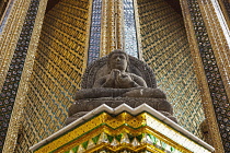 Thailand, Bangkok, Grand Palace, Seated stone Buddha statue with shiny, golden yellow glass mosaic behind it.