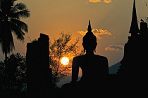 Thailand, Sukothai, Seated Buddha and stupa silhouetted against the setting sun, Wat Mahathat Royal Temple.