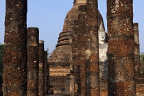 Thailand, Sukothai, White, seated Buddha, between rows of pillars and with a red-brick stupa behind it, at sunset, Wat Sra Sri.