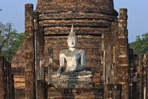 Thailand, Sukothai, White, seated Buddha, between rows of pillars and with a red-brick stupa behind it, at sunset, Wat Sra Sri.