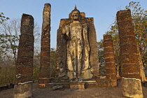 Thailand, Sukothai, Standing Buddha in forest setting, with smaller seated Buddha at base, Wat Saphan Hin.
