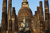 Thailand, Sukothai, White, seated Buddha, between rows of pillars and with a red-brick stupa behind it, at sunset, Wat Sra Sri.