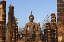 Thailand, Sukothai, Stone pillars leading up to a seated Buddha, with stupa in background, all lit by warm glow of setting sun, Wat Mahathat Royal Temple.