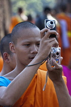 Thailand, Sukothai, Novice Buddhist monk taking photographs, holding his camera as well as a friend's, Wat Mahathat Royal Temple.