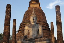 Thailand, Sukothai, White, seated Buddha, between rows of pillars and with a red-brick stupa behind it, at sunset, Wat Sra Sri.