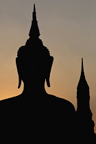 Thailand, Sukothai, Head and shoulders of seated Buddha, and tower in the background, silhouetted against sunset sky, Wat Mahathat Royal Temple.
