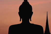 Thailand, Sukothai, Head of seated Buddha and top of nearby stupa silhouetted agaist sunset sky, Wat Mahathat Royal Temple.