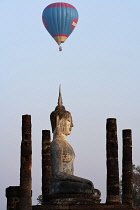 Thailand, Sukothai, Hot-air balloon floating above white, seated Buddha at dusk, Wat Mahathat Royal Temple.