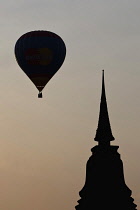 Thailand, Sukothai, Hot-air balloon and stupa top silhouetted against the sunset, Wat Mahathat Royal Temple.