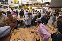 Shimbsahi, Outside Shimbashi JR station, large group of men, all over fifty years old, playing Shogi, Japanese chess, on large boards with large pieces, all standing, other men watch.