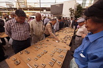 Shimbashi, Outside Shimbashi JR station, large group of men, all over fifty years old, playing Shogi, Japanese chess, on large boards with large pieces, all standing, other men watch.