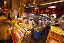 Japan, Kyoto, Nishiki Market on Nishikikoji-dori, businessman looks at display of shop specializing in tamago maki, a rolled omlette, inside the narrow shop more than a dozen staff in white smocks and...