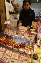 Japan, Kyoto, Nishiki Market on Nisiki koji-dori street, signs in English and Japanese, at a fish shop, sashimi on a stick for a quick snack.