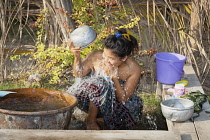 Myanmar, Mandalay, Young woman washing herself outside her house, Yay Kyi village