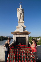Spain, Andalucia, Cordoba, Worshippers light candles at the base of the statue of San Rafael patron saint of Cordoba on the Roman Bridge.