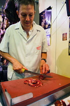 Spain, Andalucia, Seville, A butcher uses a knife to cut slices of chorizo in the market at Metropol Parasol.