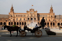 Spain, Andalucia, Seville, Plaza de Espana with horse-drawn carriages for hire in shadow in the foreground.
