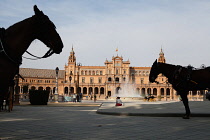 Spain, Andalucia, Seville, Plaza de Espana with horse-drawn carriages for hire in shadow in the foreground.