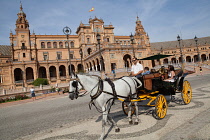 Spain, Andalucia, Seville, Plaza de Espana with horse-drawn carriage taking tourists for a ride in the foreground.
