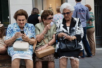 Spain, Andalucia, Seville, Women in the Triana district converse on a bench in Calle SanJacinto as another gets to grips with mobile technology.