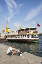 Turkey, Istanbul, Man fishing on quayside, and passenger ferry in Karakoy Cruise Terminal, Bosphorus Strait.