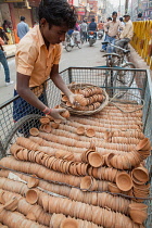 India, Uttar Pradesh, Varanasi, A deliveryman unloads clay cups, used to serve chai, from a bicycle trailer.