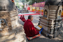 India, Bihar, Bodhgaya, Monk praying before a statue of the Buddha set in a stupa at the Mahabodhi Temple in Bodhgaya.