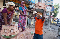 India, Telengana, Hyderabad, Labourers load bricks onto trays to carry on their heads.