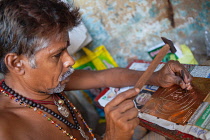 India, Tamil Nadu, Madurai, A tinker engraving a brass sheet in his workshop in Madurai.