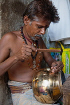 India, Tamil Nadu, Madurai, A tinker engraving a brass pot in his workshop in Madurai.