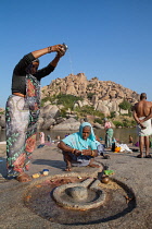 India, Karnataka, Hampi, Pilgrims make an offering at a lingam beside the Tungabhadra River in Hampi.