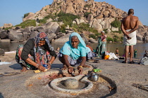 India, Karnataka, Hampi, Pilgrims make an offering at a lingam beside the Tungabhadra River in Hampi.