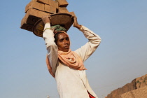 India, Karnataka, Harihar, Labourer carrying bricks on her head at a brick factory in Harihar.