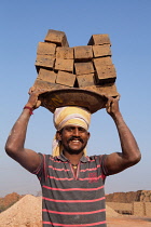 India, Karnataka, Harihar, Portrait of a labourer carrying bricks on his head at a brick factory in Harihar.