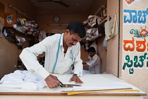 India, Karnataka, Hassan, A tailor cutting cloth at his shop in Hassan.