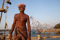 India, Kerala, Fort Cochin, Portrait of a fisherman with the Chinese fishing nets in the background.