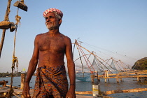 India, Kerala, Fort Cochin, Portrait of a fisherman with the Chinese fishing nets in the background.