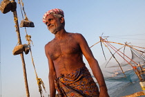 India, Kerala, Fort Cochin, Portrait of a fisherman with the Chinese fishing nets in the background.