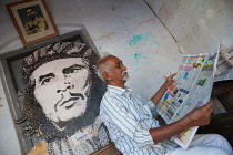 India, Kerala, Fort Cochin, Man reading a newspaperwith an image of Che Guevara in the background.