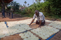 India, Kerala, Varkala, A man spreads out circular pieces of thin rolled dough to dry in the sun.