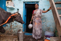 India, Karnataka, Bijapur, Portrait of a woman in the doorway of her home with cattle in the front yard.