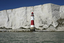 England, East Sussex, Beachy Head, Red and white painted lighthouse at base of cliffs.