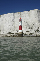 England, East Sussex, Beachy Head, Red and white painted lighthouse at base of cliffs.