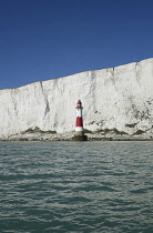 England, East Sussex, Beachy Head, Red and white painted lighthouse at base of cliffs.