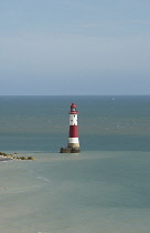England, East Sussex, Beachy Head, Red and white painted lighthouse at base of cliffs.