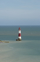 England, East Sussex, Beachy Head, Red and white painted lighthouse at base of cliffs.