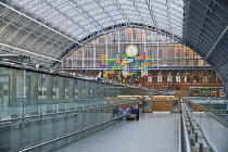 England, London, St Pancras railway station on Euston Road, man with suitcase sits on concourse awaiting his train.