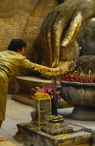Thailand, Sukothai, Woman burning incense before giant, Buddha.